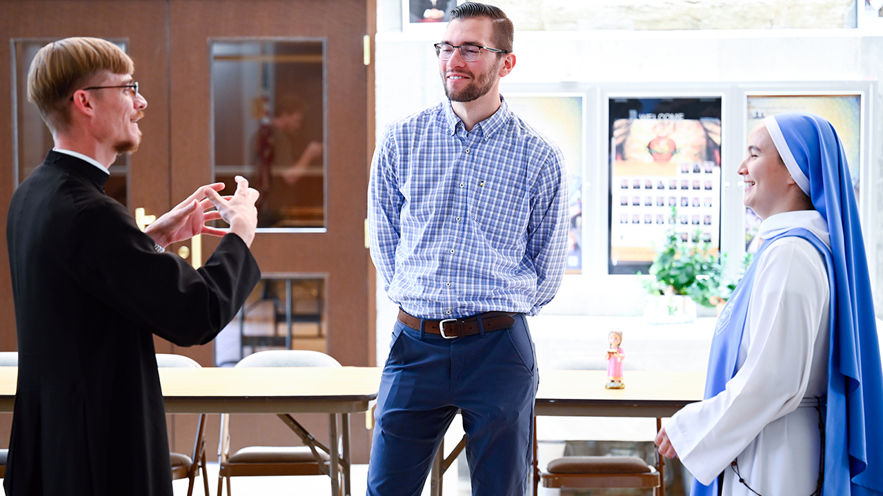 Image of three people smiling and watching a young priest talk